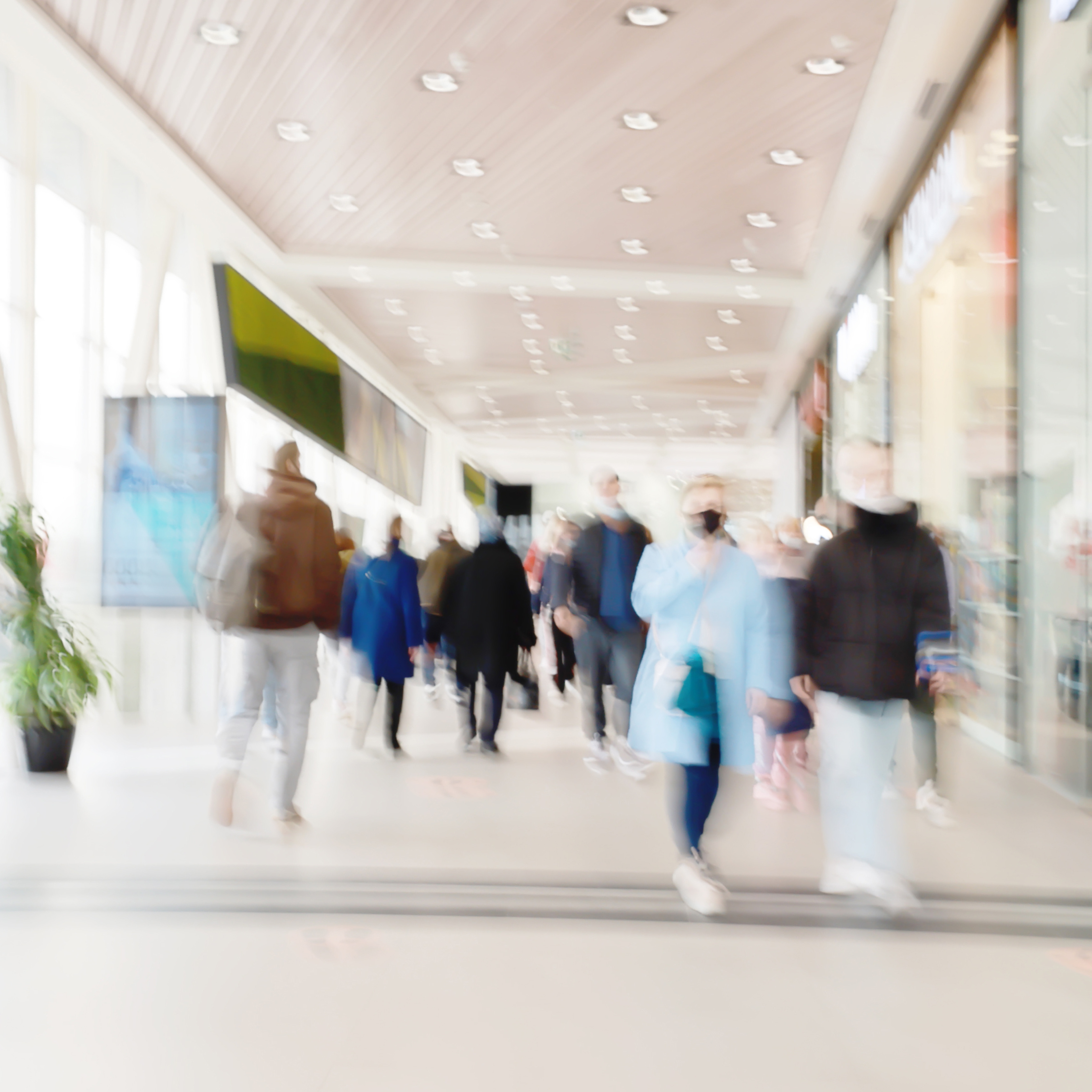 People walking through a bright indoor hallway with glass walls and shops.