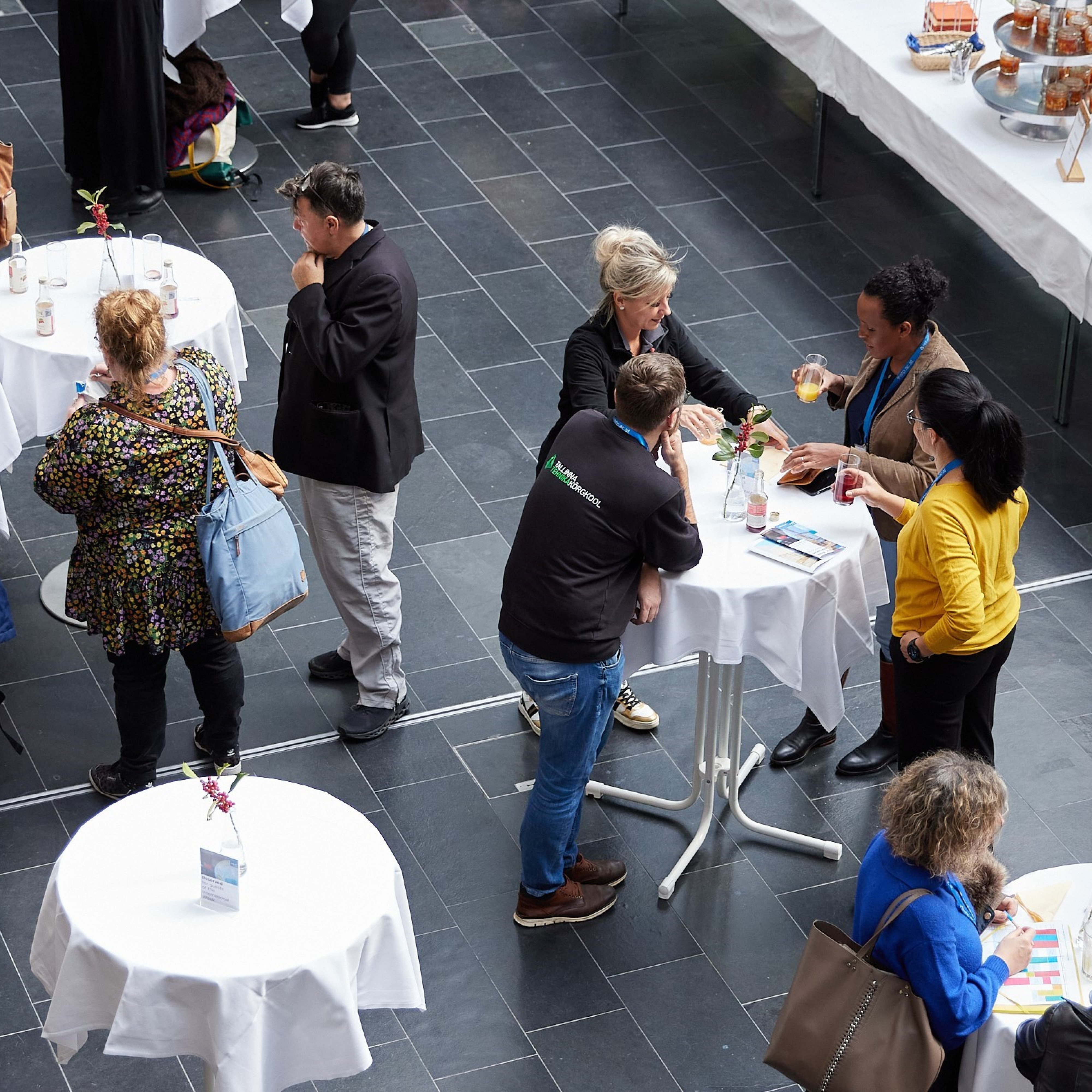 People gathered around standing tables at a networking event with food and drinks.