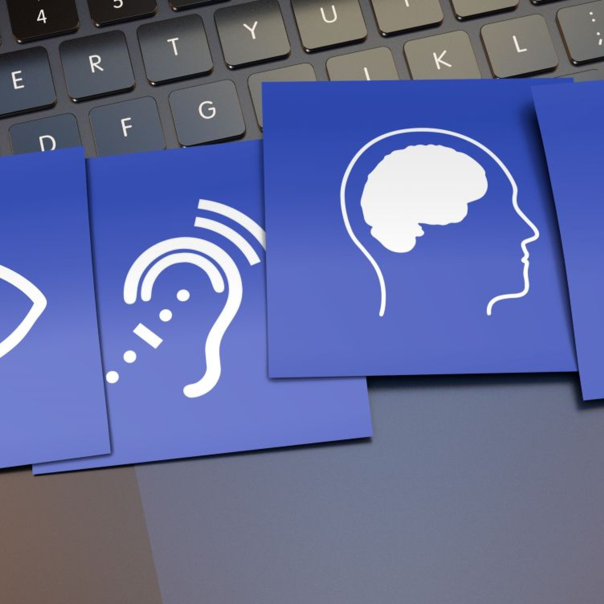 Four blue cards laying on top of a black laptop keyboard. The cards show the accessibility symbols for visual impairment, hearing impairment, cognitive impairment and a wheelchair.